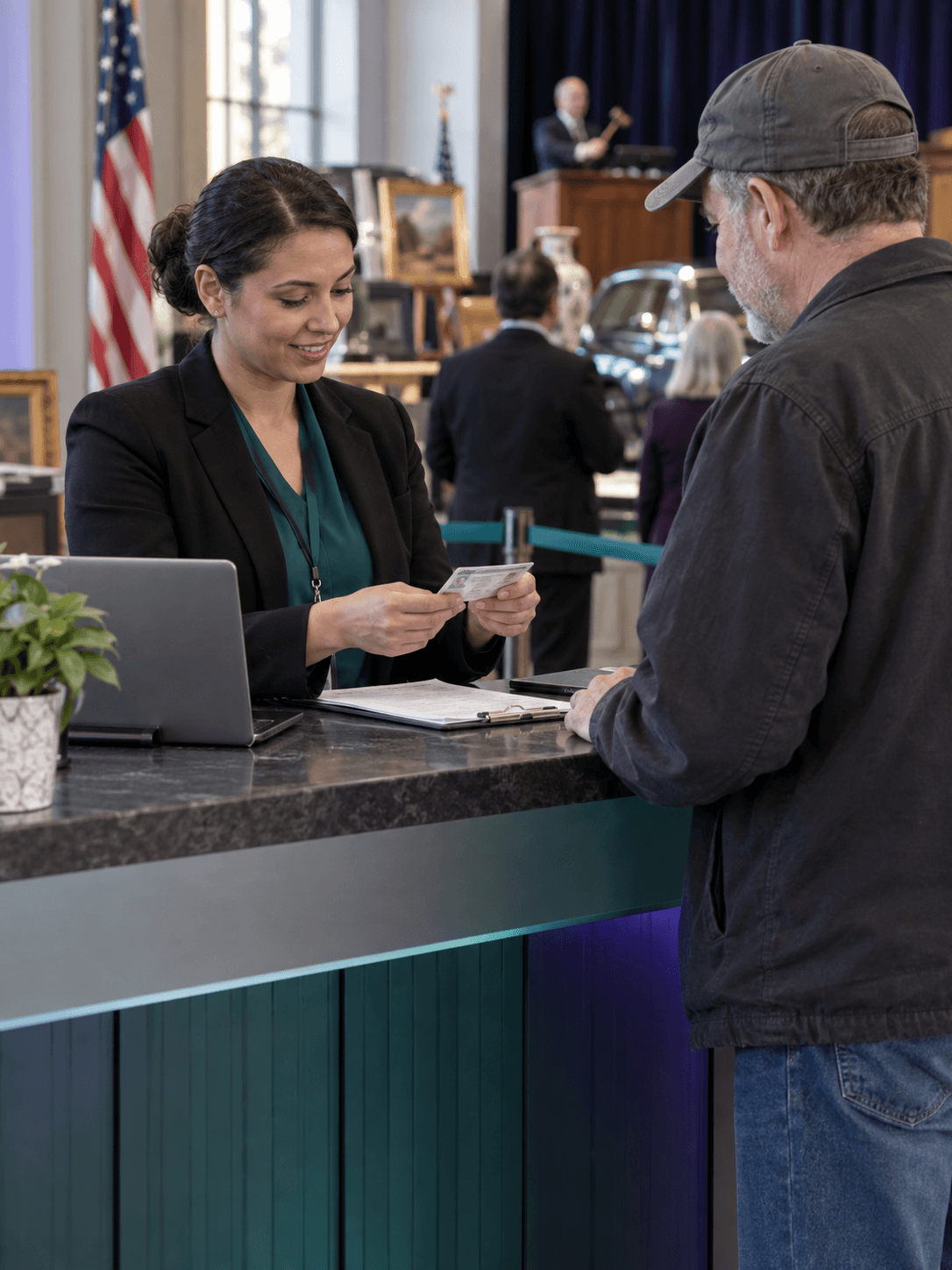 A public auction registration clerk checks bidder identification paperwork across a civic service counter