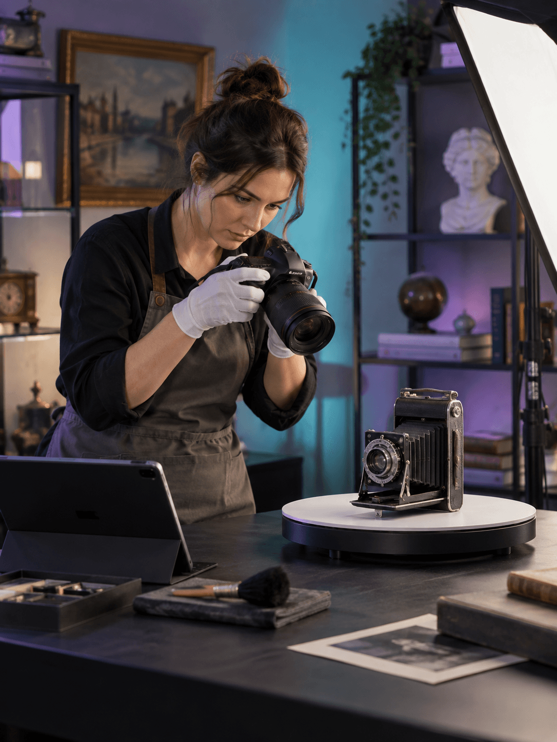 A catalog assistant photographs a vintage mechanical camera on a studio turntable with careful lighting and a tablet nearby